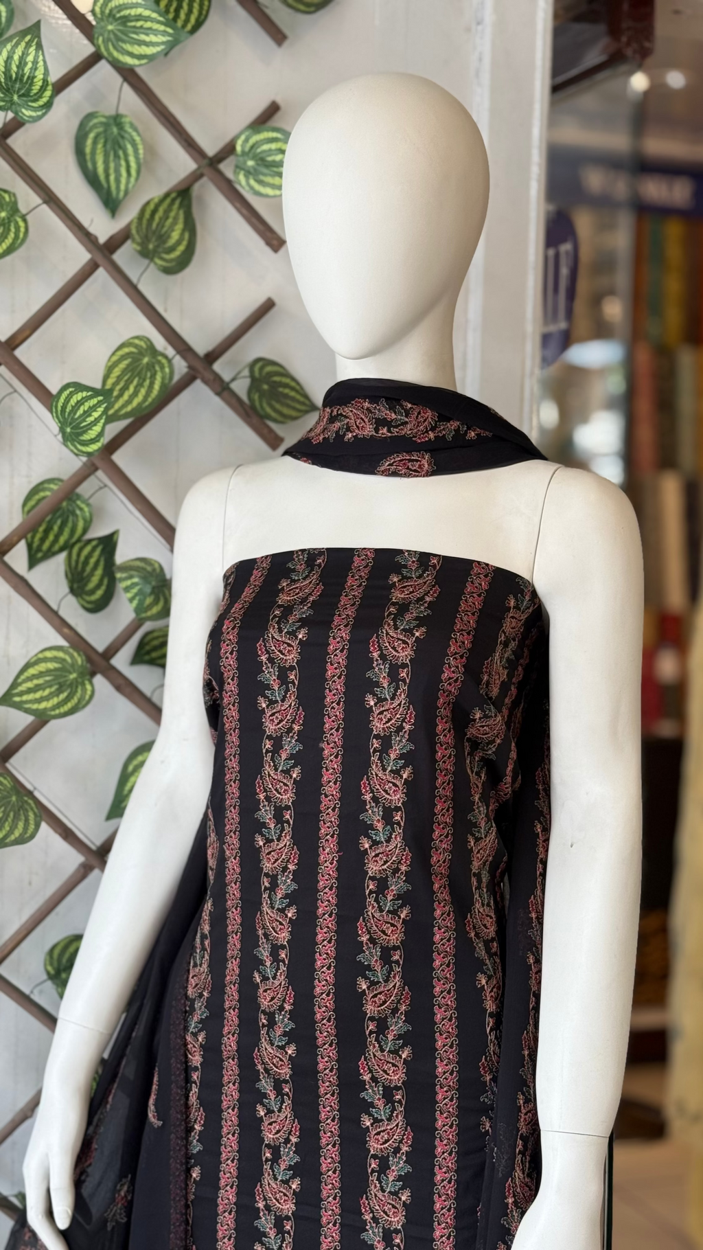 Mannequin wearing a black and red patterned garment with a decorative background.